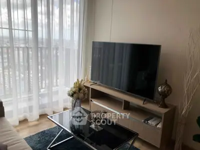 Modern living room with large TV, glass coffee table, and city view through sheer curtains.
