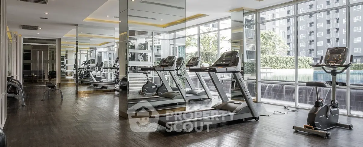 Modern gym with treadmills and mirrored walls in luxury apartment complex.