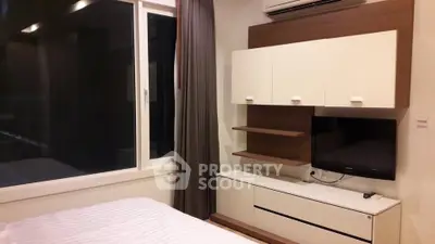 Modern bedroom with sleek furniture and large window, featuring a wall-mounted TV and air conditioning.