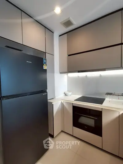 Modern kitchen with sleek cabinetry and built-in appliances, featuring a black refrigerator and electric cooktop.