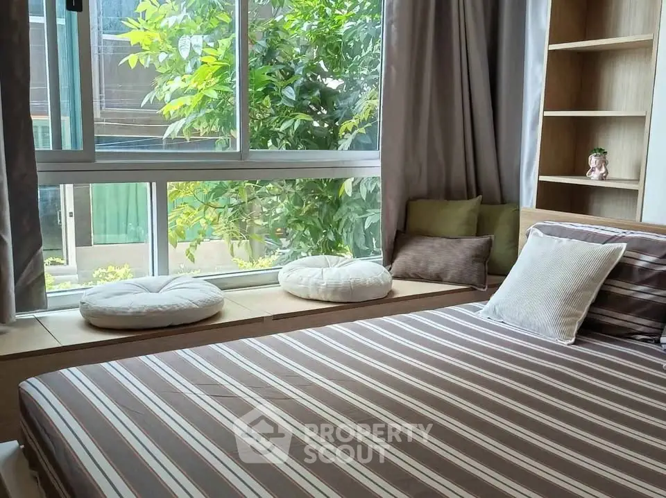 Cozy bedroom with large window and garden view, featuring stylish striped bedding and comfortable seating area.