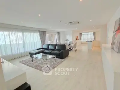 Spacious modern living room with sleek black sofa and large windows in a bright open-plan layout.