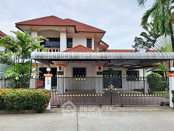 Charming two-story house with red roof and gated entrance in lush tropical setting.