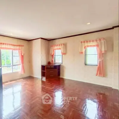 Spacious sunlit room with elegant wooden flooring and charming window drapes.