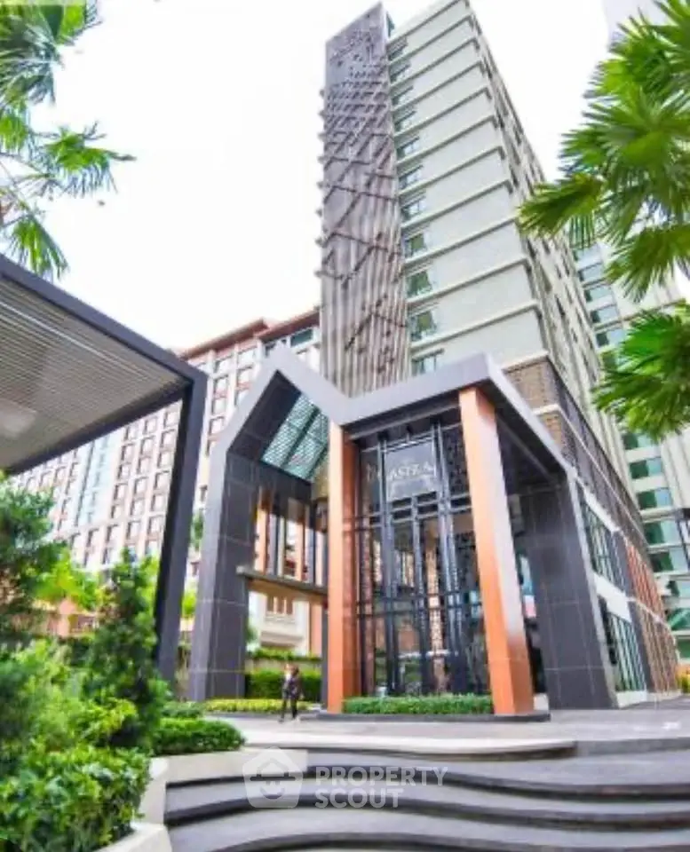 Modern high-rise building entrance with sleek architectural design and lush greenery.