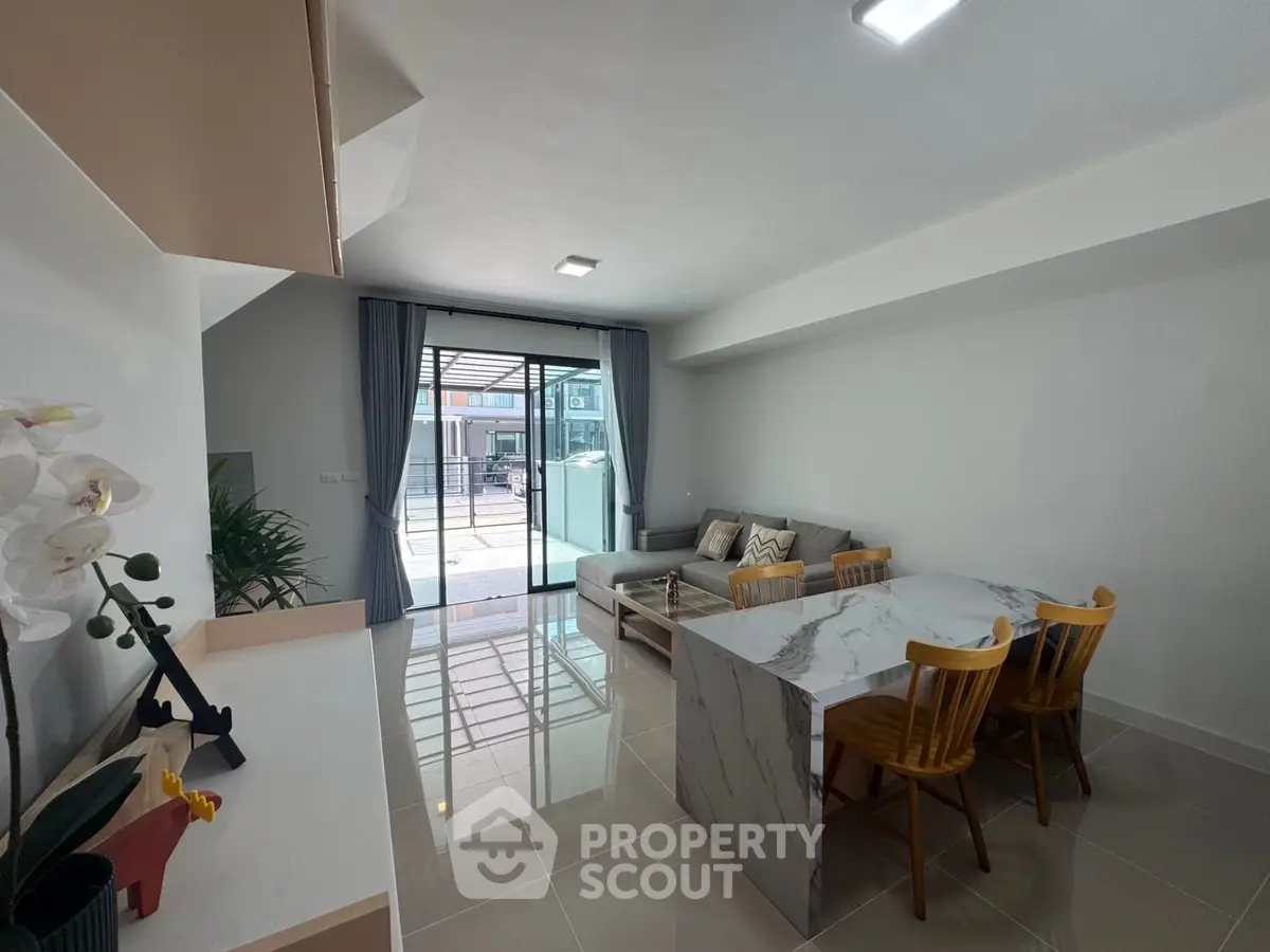 Modern living room with marble dining table and cozy seating area, featuring large windows for natural light.