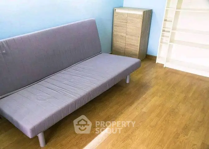 Minimalist room with a sleek gray futon and wooden flooring, perfect for modern living.