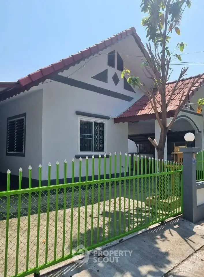 Charming single-story house with red roof and green fence, perfect for family living.