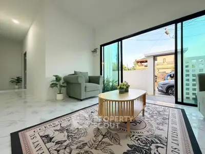 Spacious modern living room with large glass doors opening to a sunny patio, featuring stylish furniture and elegant decor.