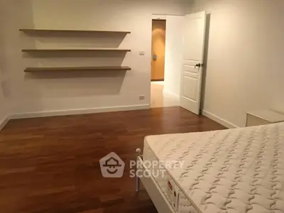 Spacious bedroom with wooden floors and open shelves, perfect for modern living.