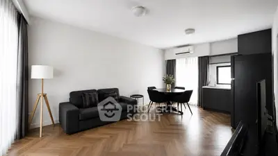 Modern living room with sleek black furniture and wooden flooring, featuring a cozy dining area and natural light.