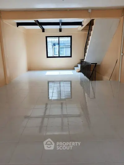 Spacious open-plan living area with staircase and large window, perfect for modern living.
