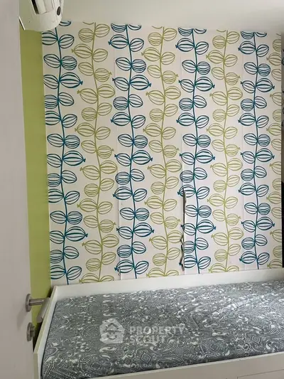 Charming bedroom with vibrant leaf-patterned wallpaper and cozy bed setup.