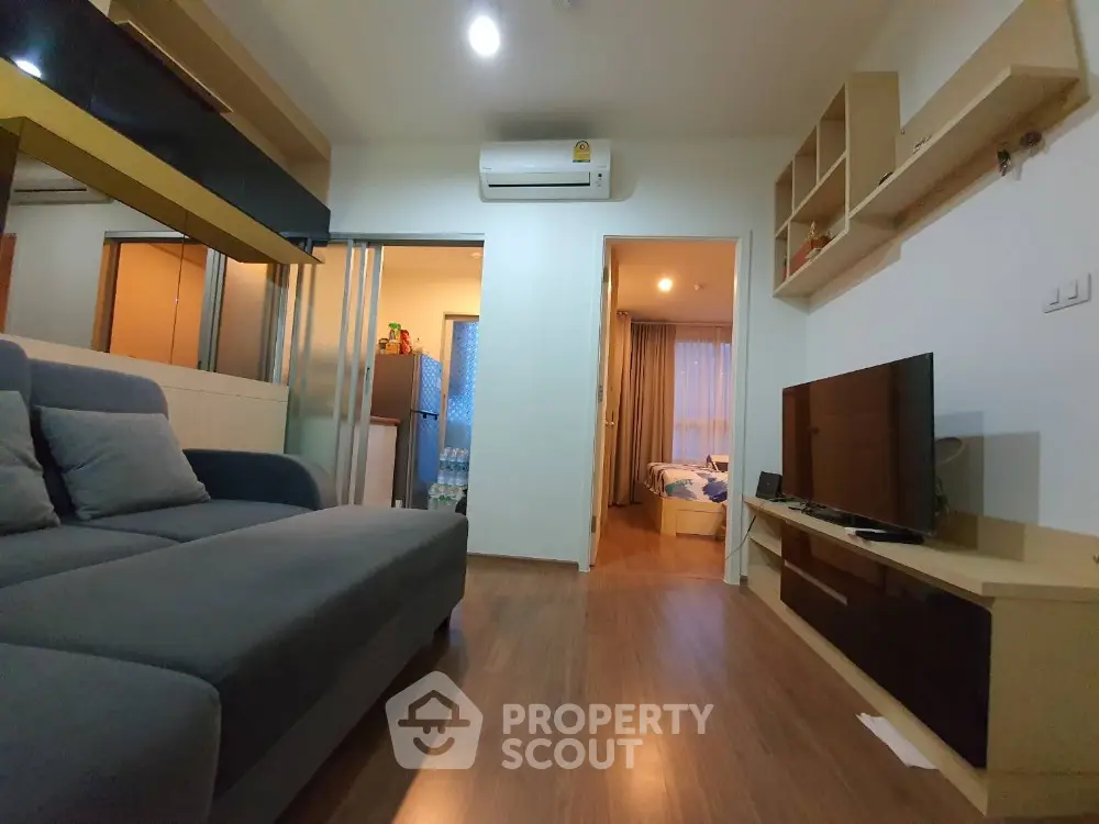 Modern living room with cozy sofa and wall-mounted TV, leading to a bedroom with natural light.