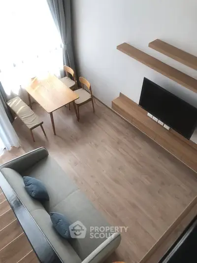 Modern living room with wooden flooring, sleek furniture, and natural light from large window.