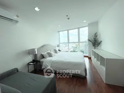 Spacious bedroom with large windows offering stunning city views, modern furnishings, and elegant decor.
