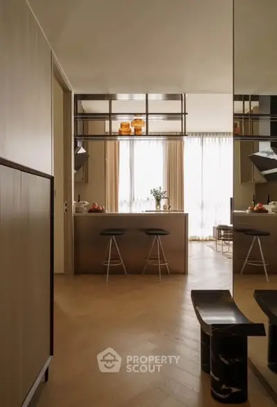Modern kitchen with island and bar stools, elegant lighting, and wooden flooring.