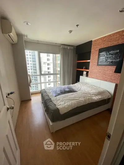 Modern bedroom with large window and city view, featuring wooden flooring and stylish decor.