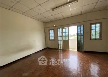 Spacious empty room with wooden flooring and large windows for natural light.