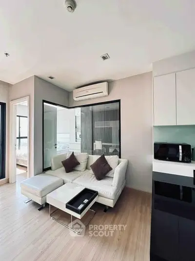 Modern living room with sleek design, featuring a cozy white sofa, stylish decor, and open layout kitchen.