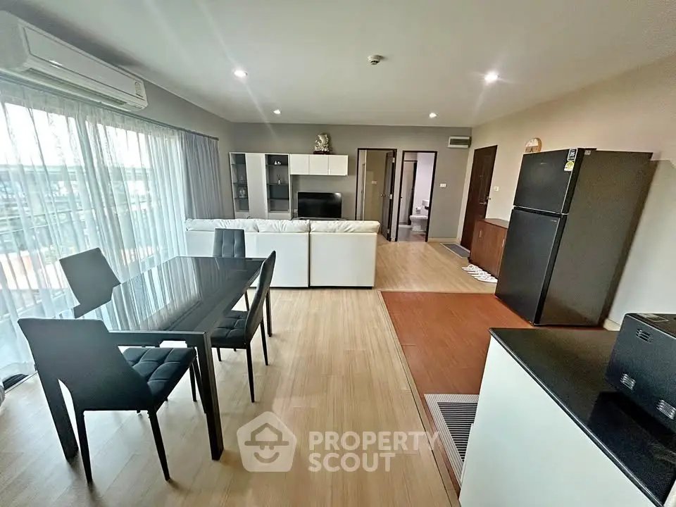 Spacious modern living room with open kitchen and dining area, featuring sleek furniture and natural light.