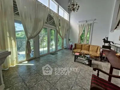 Spacious living room with high ceilings and elegant decor, featuring large windows and a garden view.
