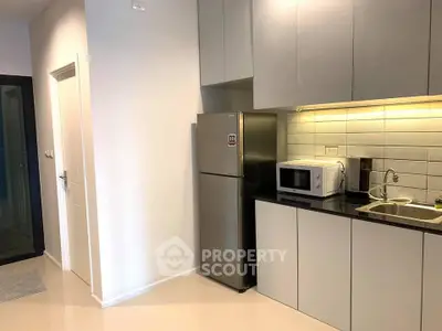 Modern kitchen with sleek cabinets, stainless steel fridge, and microwave in stylish apartment.