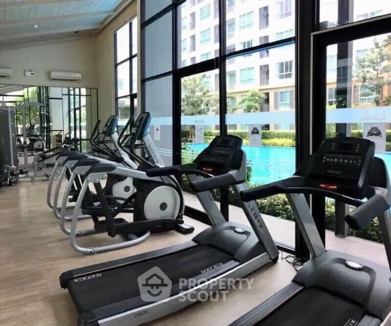 Modern gym with treadmills overlooking a pool in a luxury apartment complex.