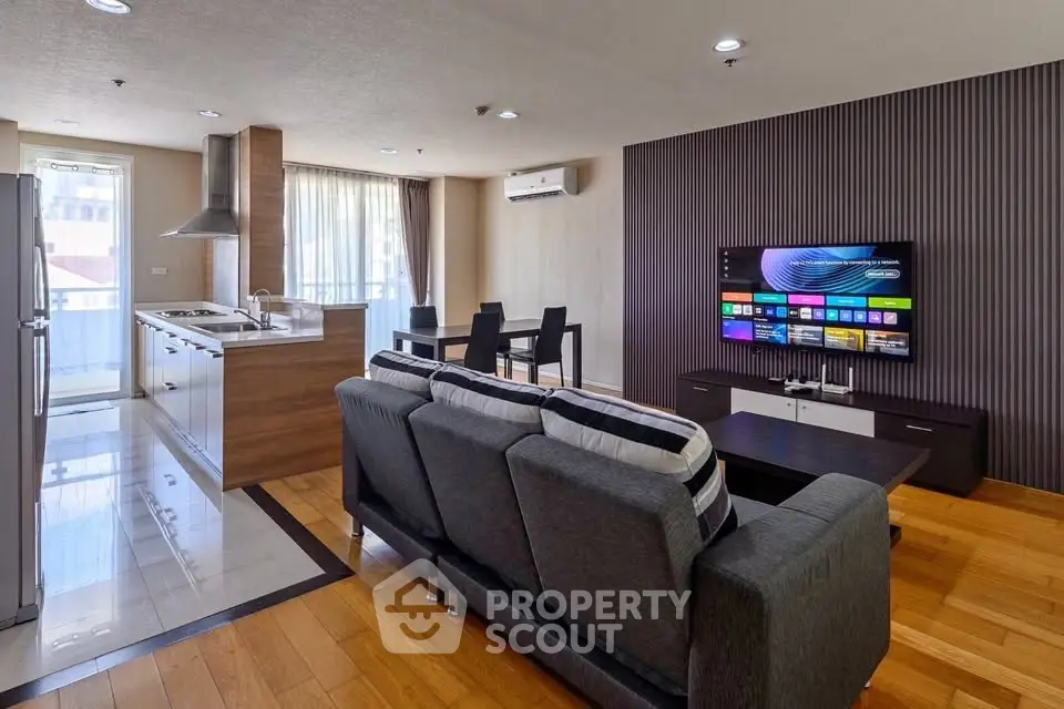 Modern open-plan living room with sleek kitchen and dining area, featuring a large TV and stylish decor.