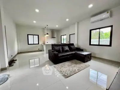 Spacious modern living room with sleek black sofa and open kitchen layout.