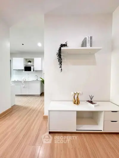 Modern minimalist living space with sleek white furniture and open kitchen layout.