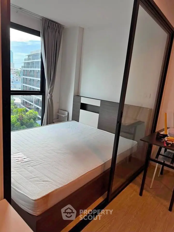 Modern bedroom with large window and sliding glass door, offering city views and natural light.