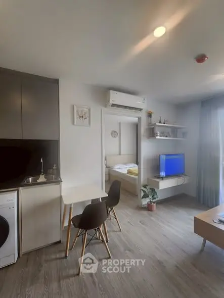 Modern open-plan living room with kitchen and bedroom view, featuring sleek furniture and natural light.