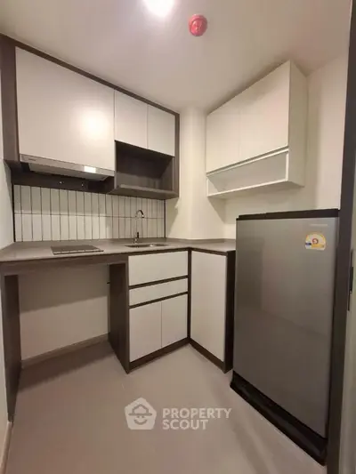Modern kitchen with sleek cabinetry and compact fridge in a stylish apartment.