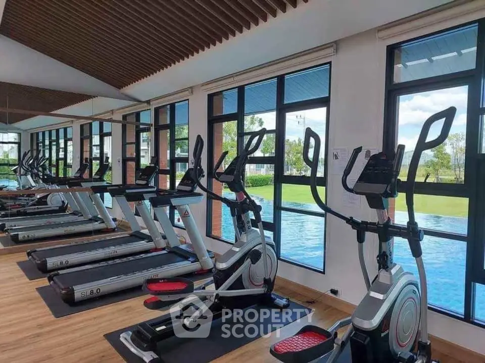 Modern gym with treadmills and elliptical machines overlooking a scenic pool view.