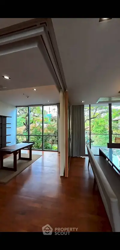 Spacious living room with large windows and wooden flooring, offering a serene garden view.