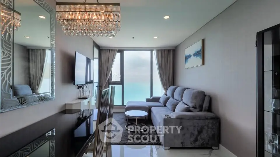Luxurious living room with ocean view, elegant chandelier, and plush gray sofa.
