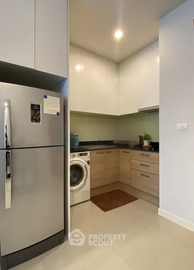 Modern kitchen with sleek cabinets, fridge, and washing machine in a compact layout.