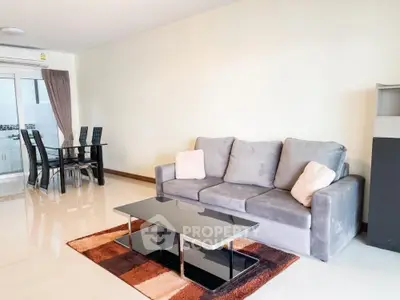 Spacious living room with glossy tiled floors, modern grey sofa, elegant glass coffee table, and a sleek dining set by the window, exuding contemporary charm.