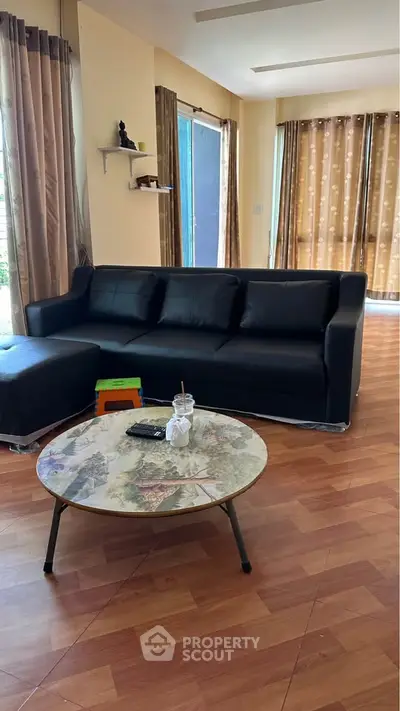 Spacious living room with modern black sofa and stylish coffee table, featuring large windows with elegant curtains.