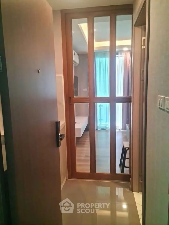 Modern apartment entrance with wooden door and glass panels leading to a bright living area.