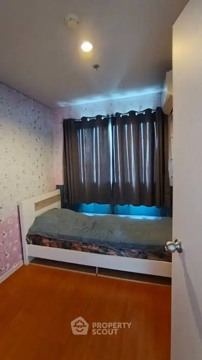 Cozy bedroom with floral wallpaper and wooden flooring, featuring a single bed and dark curtains.