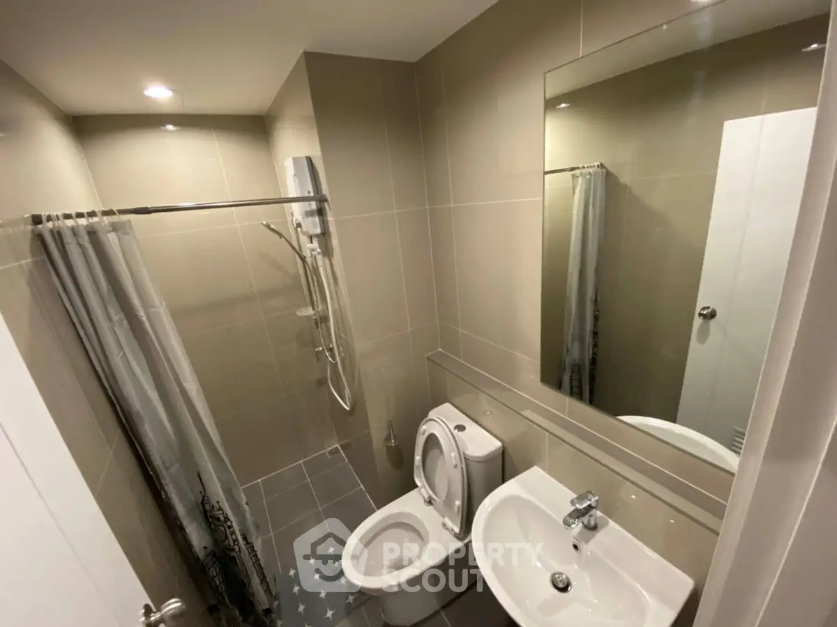 Modern bathroom with sleek fixtures and neutral tiles, featuring a shower and toilet.