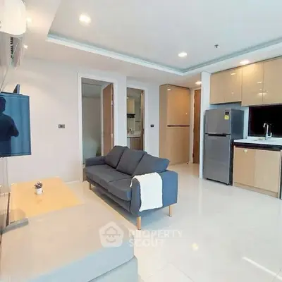 Modern living room with open kitchen, featuring sleek appliances and cozy seating area.