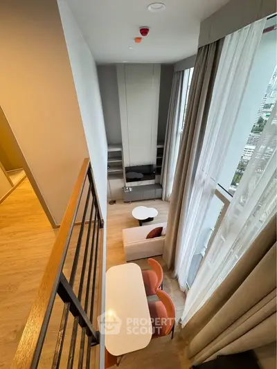 Modern loft-style living room with high ceilings and large windows offering city views.