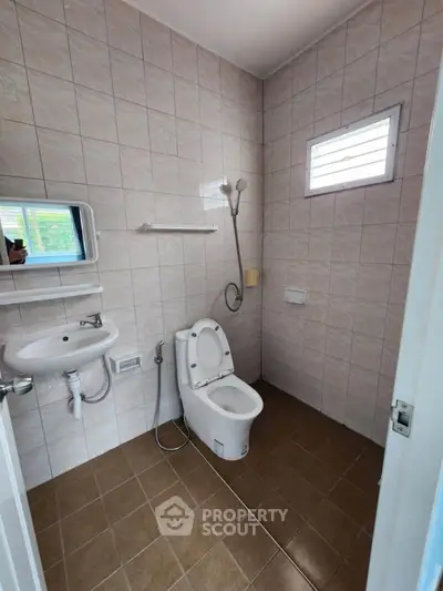 Compact bathroom with modern fixtures and tiled walls, featuring a window for natural light.