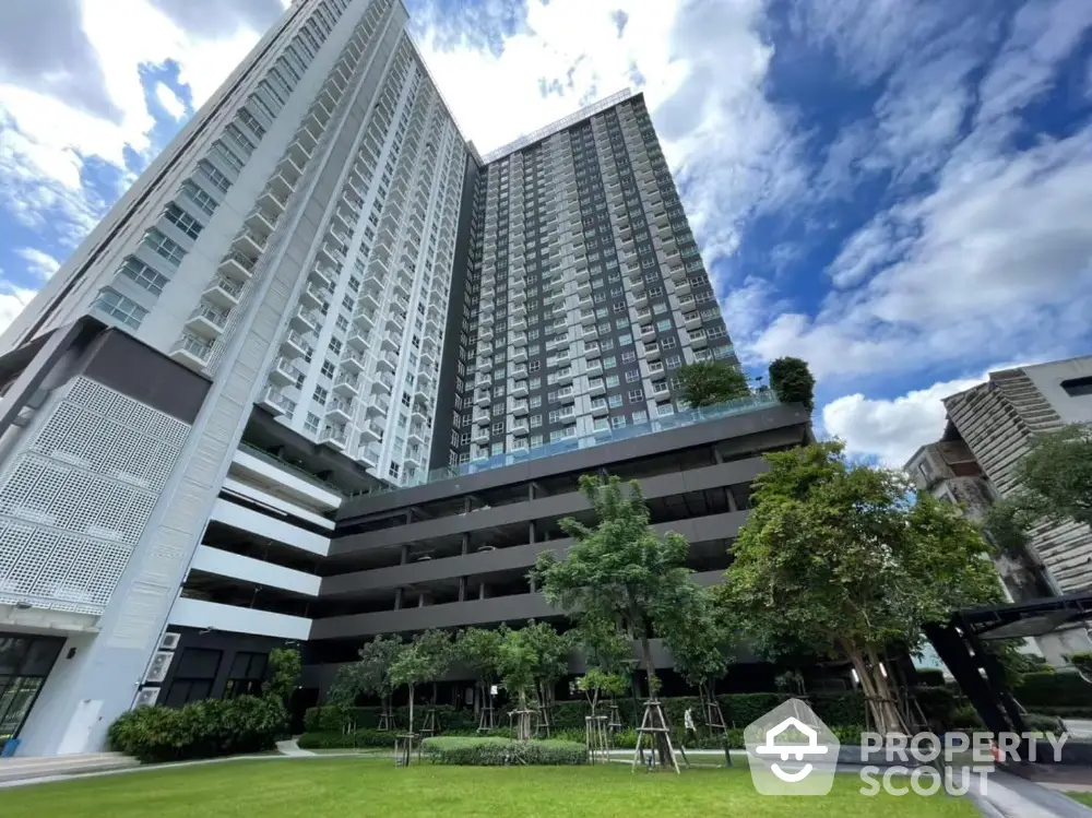 Modern high-rise residential building with lush green garden and clear blue sky.