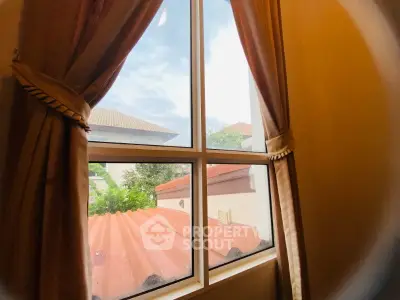 Charming window view with lush greenery and rooftops, perfect for serene living.