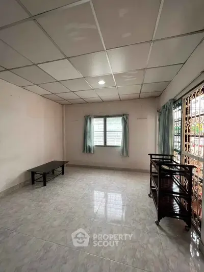 Spacious living room with tiled flooring and natural light from large windows.