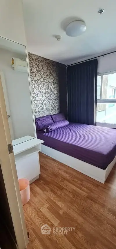 Cozy bedroom with elegant wallpaper and large window, featuring a comfortable bed and wooden flooring.